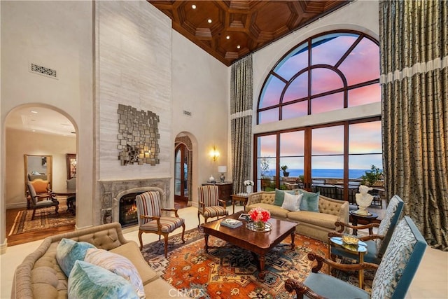 living area featuring arched walkways, a high ceiling, a warm lit fireplace, and visible vents