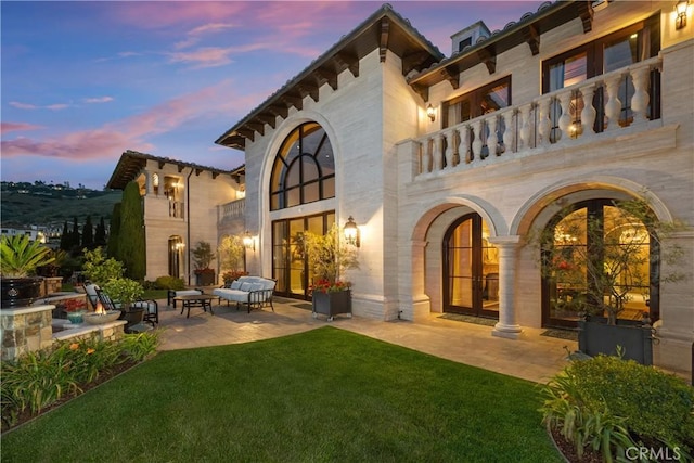 back of house at dusk with french doors, a balcony, a yard, a patio, and outdoor lounge area