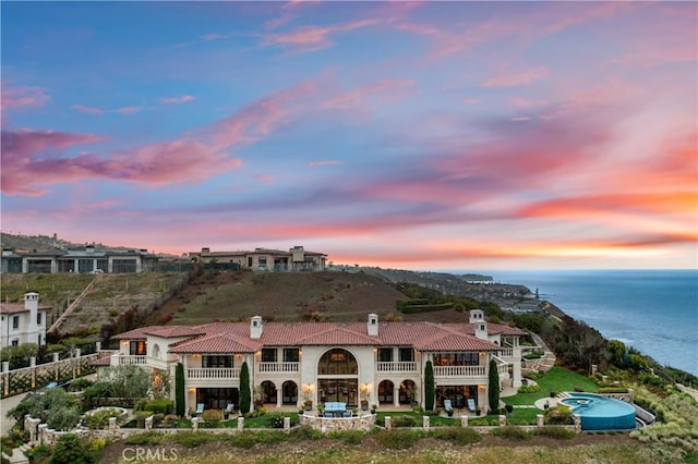 exterior space with a water view, a chimney, a tile roof, and a balcony
