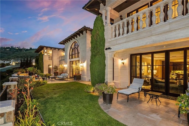 rear view of property featuring a patio, french doors, a balcony, and a yard