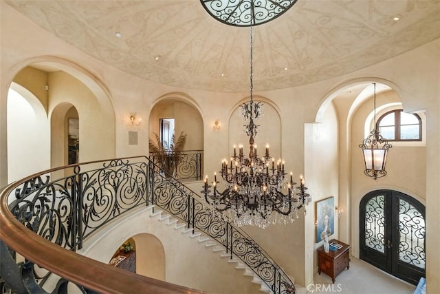 entryway featuring french doors, a towering ceiling, arched walkways, a notable chandelier, and stairs