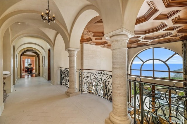hall featuring arched walkways, coffered ceiling, ornate columns, and a notable chandelier