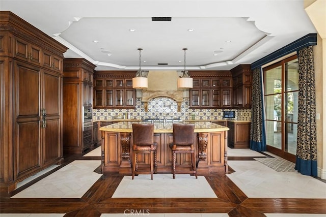 kitchen featuring glass insert cabinets, hanging light fixtures, decorative backsplash, and an island with sink