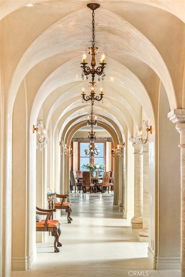 corridor with arched walkways, an inviting chandelier, and ornate columns