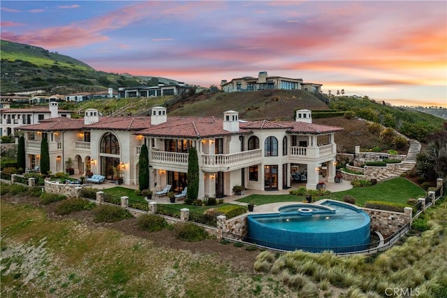 back of house with a balcony, a patio, a fenced backyard, a mountain view, and a pool with connected hot tub