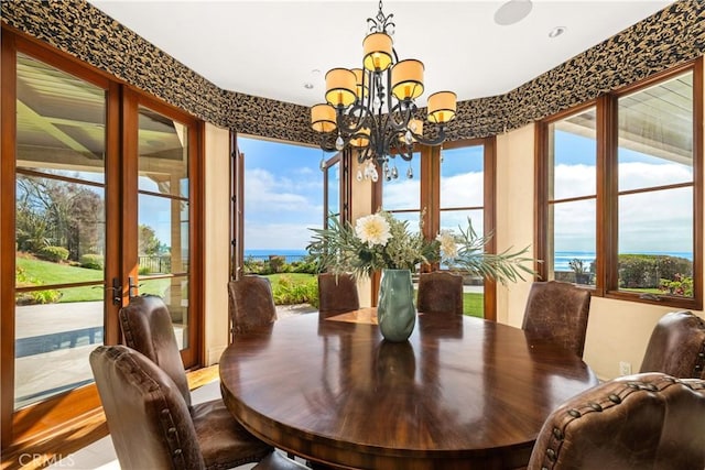 dining space with an inviting chandelier, a water view, wood finished floors, and french doors