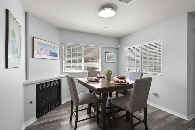dining room featuring dark wood finished floors, a glass covered fireplace, and baseboards