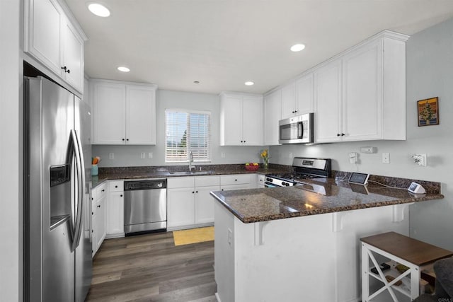 kitchen featuring stainless steel appliances, a peninsula, a sink, white cabinets, and dark wood-style floors