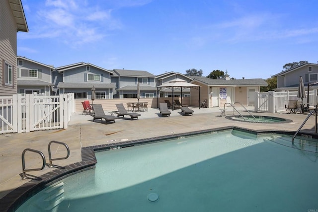 community pool featuring a gate, a hot tub, a residential view, and a patio area