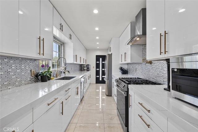 kitchen featuring wall chimney range hood, modern cabinets, a sink, light stone counters, and stainless steel appliances