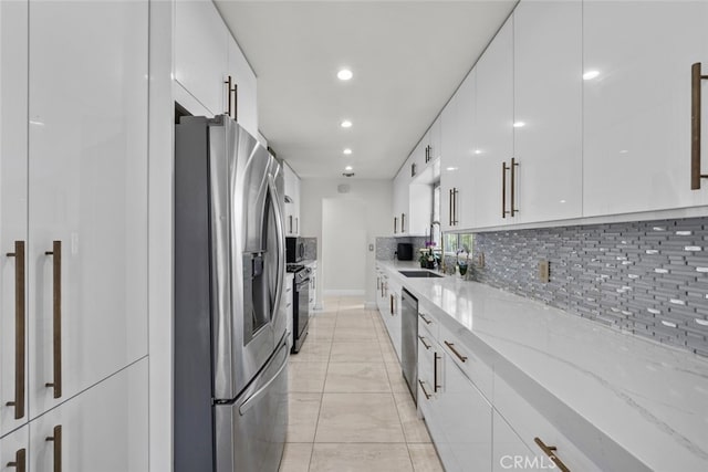 kitchen with modern cabinets, white cabinets, tasteful backsplash, light stone counters, and appliances with stainless steel finishes
