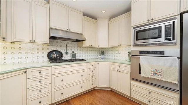 kitchen with light countertops, under cabinet range hood, cream cabinets, and stainless steel appliances