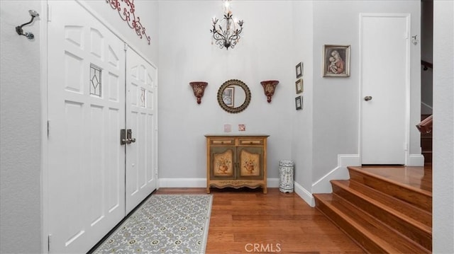 entrance foyer with baseboards, an inviting chandelier, wood finished floors, and stairway