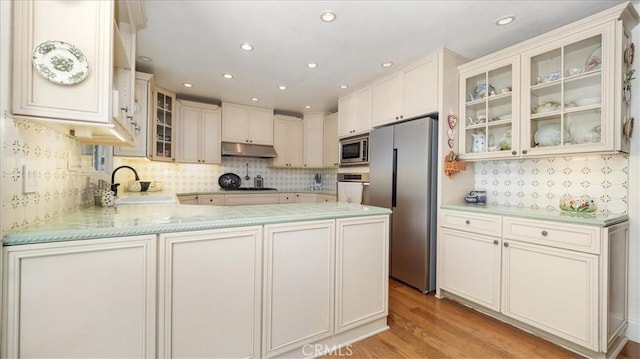 kitchen featuring appliances with stainless steel finishes, a sink, light countertops, decorative backsplash, and under cabinet range hood