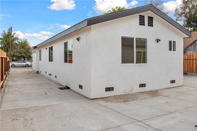 view of property exterior with crawl space, fence, a patio, and stucco siding