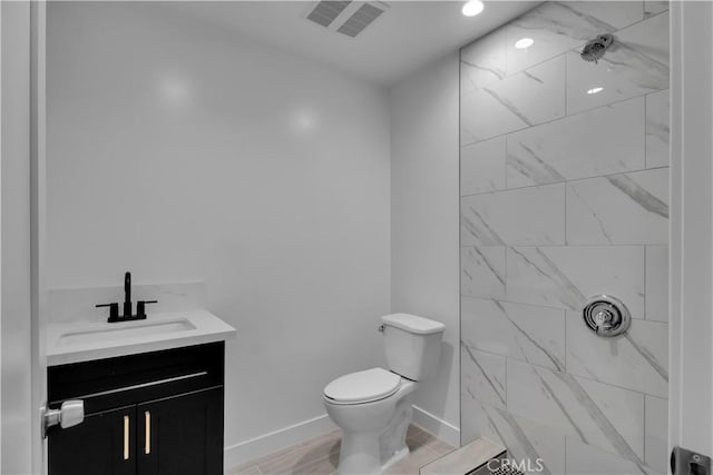 bathroom featuring visible vents, a tile shower, vanity, baseboards, and toilet