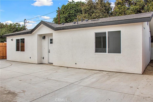 rear view of house featuring stucco siding, a shingled roof, a patio area, and fence