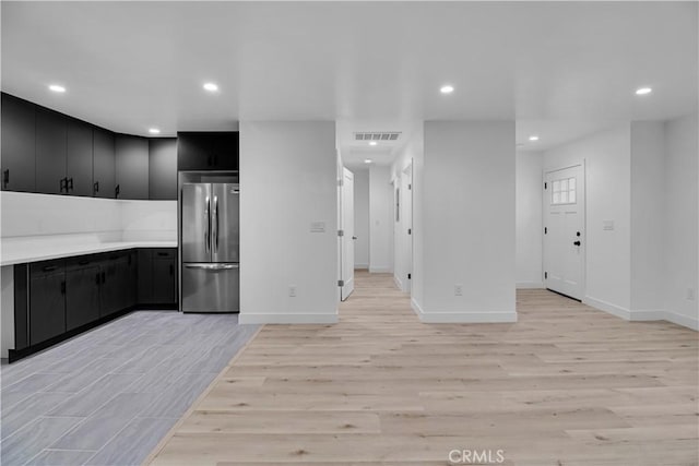 kitchen featuring freestanding refrigerator, dark cabinets, recessed lighting, and light wood-style floors