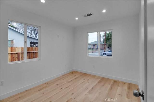 empty room with a wealth of natural light, recessed lighting, wood finished floors, and visible vents