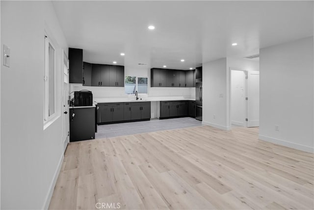 kitchen featuring a sink, light wood-style floors, light countertops, black refrigerator, and baseboards
