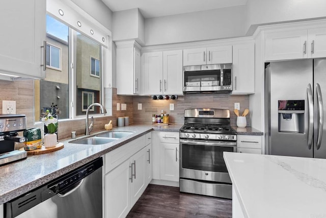 kitchen with stainless steel appliances, light stone counters, white cabinetry, and a sink