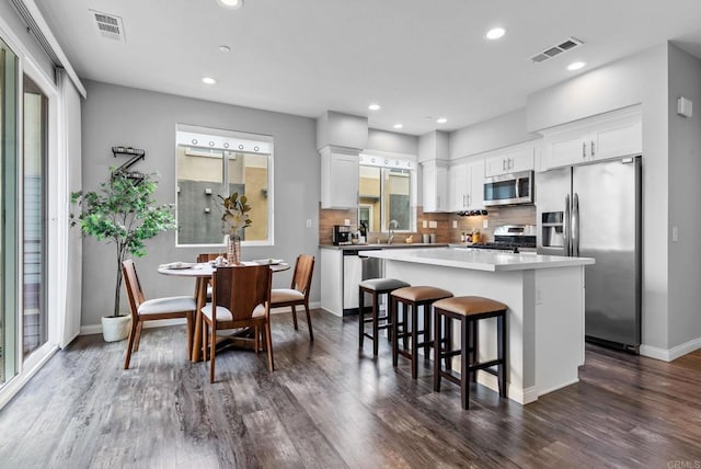 kitchen with a kitchen island, dark wood-type flooring, white cabinets, appliances with stainless steel finishes, and backsplash