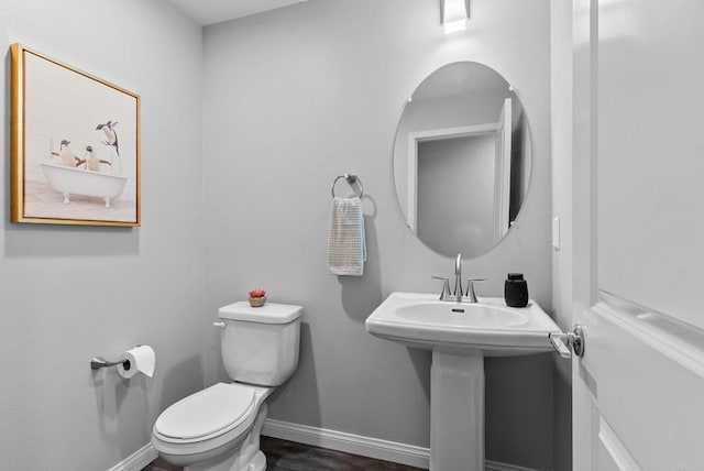 half bath with baseboards, wood finished floors, and toilet