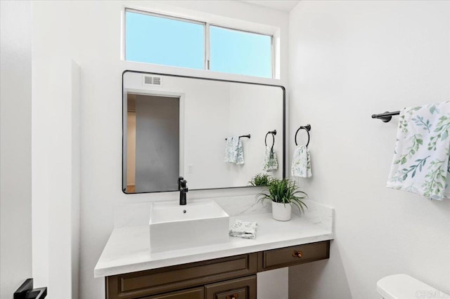 half bath featuring vanity, visible vents, and toilet