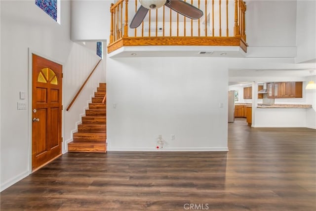 unfurnished living room featuring ceiling fan, stairs, wood finished floors, a towering ceiling, and visible vents