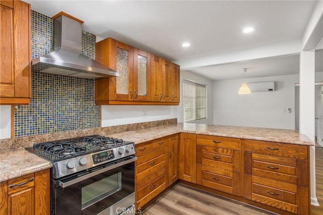 kitchen with decorative backsplash, a peninsula, wall chimney exhaust hood, stainless steel range with gas stovetop, and light wood finished floors