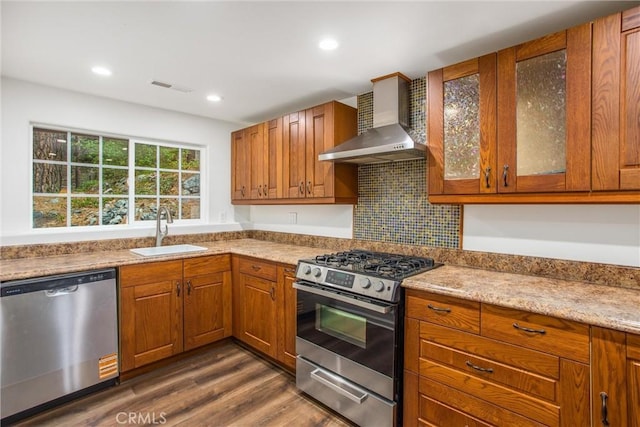 kitchen with wall chimney range hood, visible vents, a sink, glass insert cabinets, and stainless steel appliances