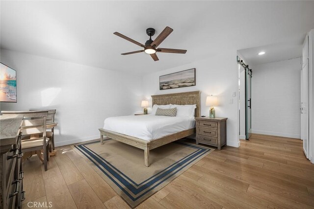 bedroom featuring a barn door, light wood finished floors, recessed lighting, baseboards, and a ceiling fan