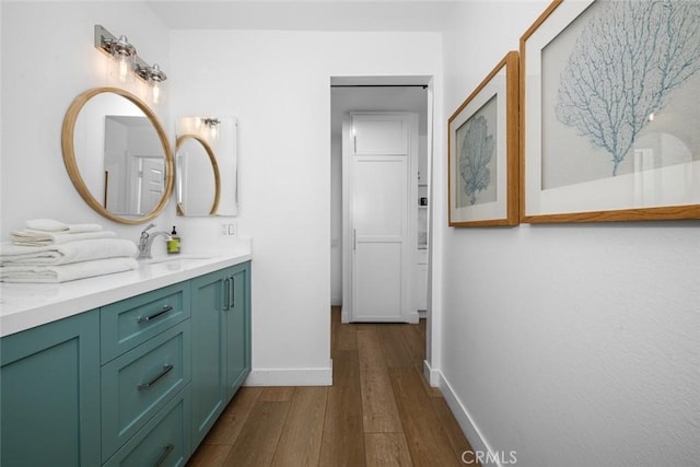 bathroom with double vanity, baseboards, a sink, and wood finished floors