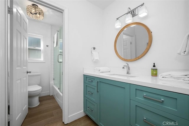 full bathroom featuring vanity, wood finished floors, toilet, baseboards, and combined bath / shower with glass door