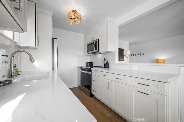 kitchen featuring light stone countertops, white cabinets, a sink, dark wood finished floors, and stainless steel appliances