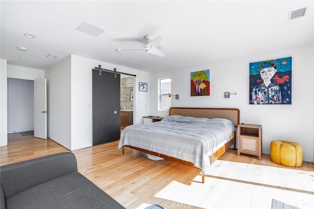 bedroom with visible vents, a barn door, a ceiling fan, and wood finished floors