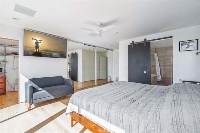 bedroom with a ceiling fan, a barn door, and wood finished floors
