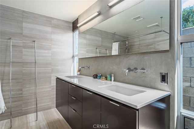 bathroom featuring a sink, tile walls, double vanity, and tiled shower