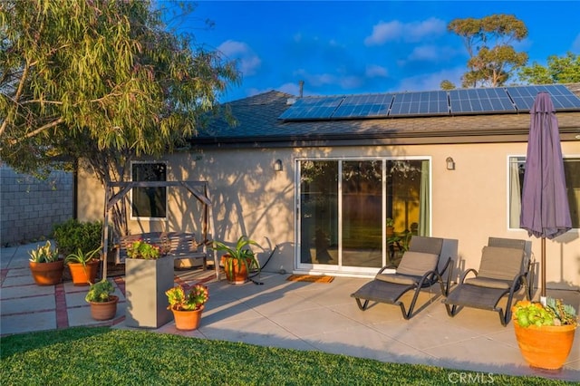 back of property featuring a patio, a shingled roof, roof mounted solar panels, and stucco siding