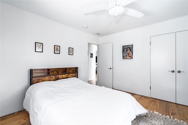 bedroom with a closet, a ceiling fan, wood finished floors, and visible vents