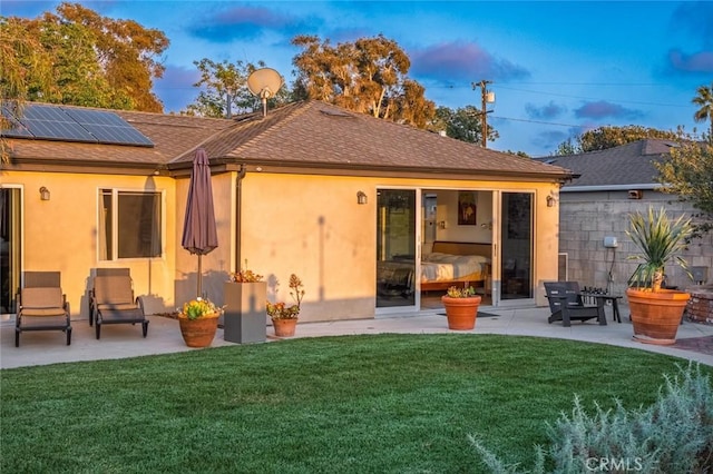 back of property with a patio, stucco siding, a shingled roof, roof mounted solar panels, and a yard