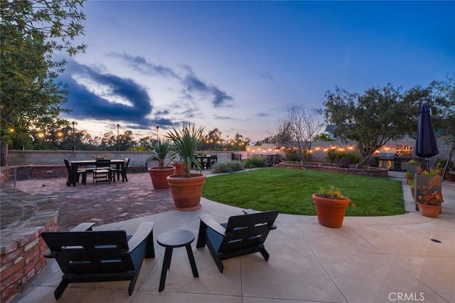 patio terrace at dusk with a fenced backyard, a yard, and outdoor dining space