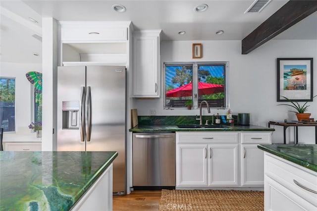 kitchen with appliances with stainless steel finishes, light wood-type flooring, a sink, white cabinets, and dark stone countertops