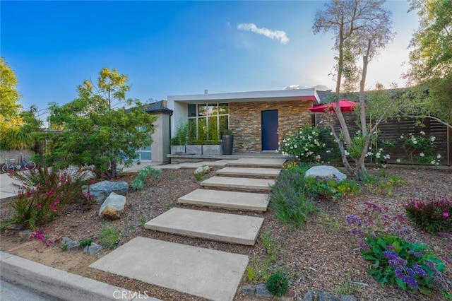 view of front of house with stucco siding, stone siding, and fence