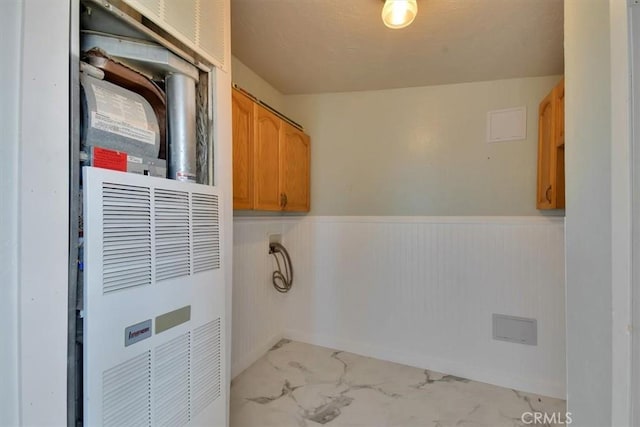laundry room with marble finish floor, cabinet space, a wainscoted wall, and a heating unit