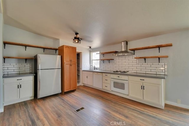 kitchen featuring wall chimney range hood, open shelves, dark countertops, white appliances, and backsplash