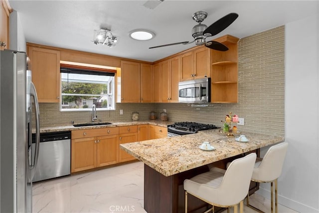 kitchen with a sink, a peninsula, marble finish floor, backsplash, and appliances with stainless steel finishes