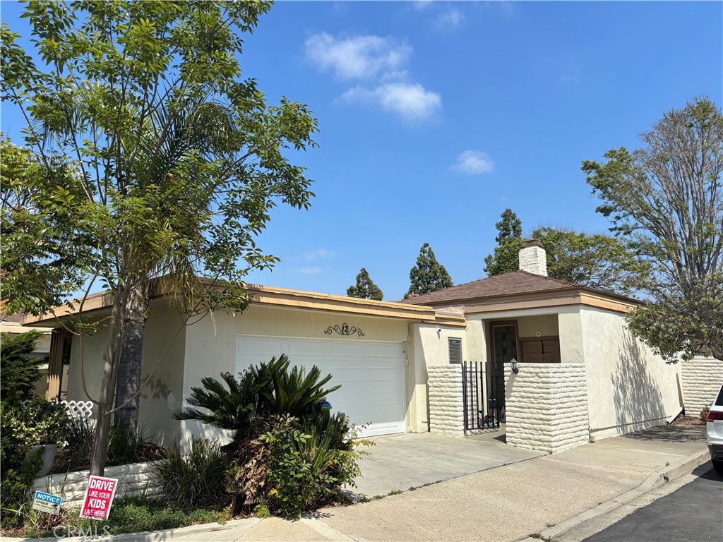 ranch-style house featuring concrete driveway, a garage, a chimney, and stucco siding