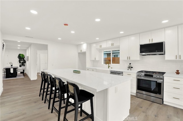 29282 Sonoma Way, San Juan Capistrano, CA 92675 - kitchen with a kitchen breakfast bar, appliances with stainless steel finishes, light wood-type flooring, a sink, and white cabinetry