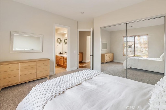 bedroom with baseboards, ensuite bathroom, light carpet, and a closet